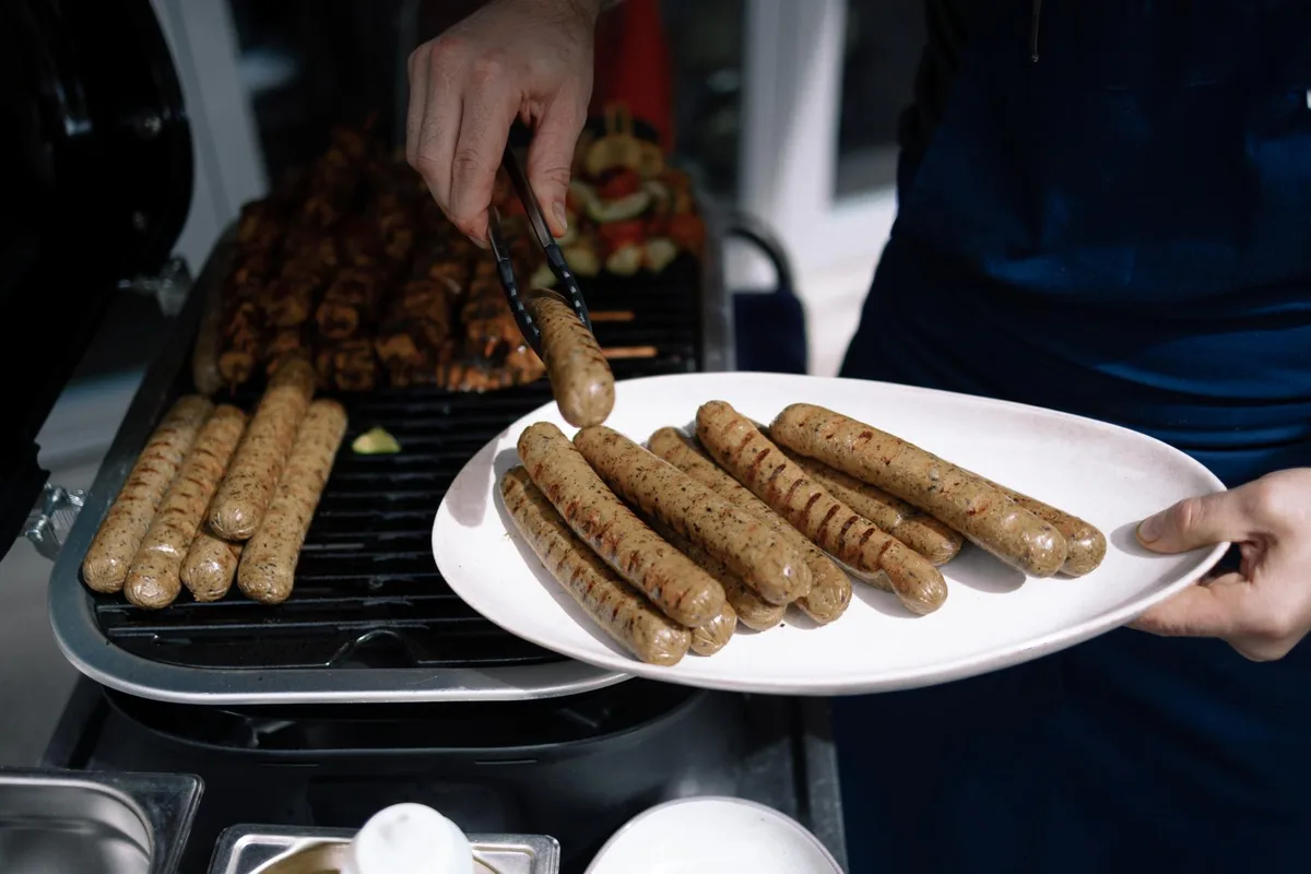 Mehrere Würste werden von einem Grill auf einen Teller gelegt.